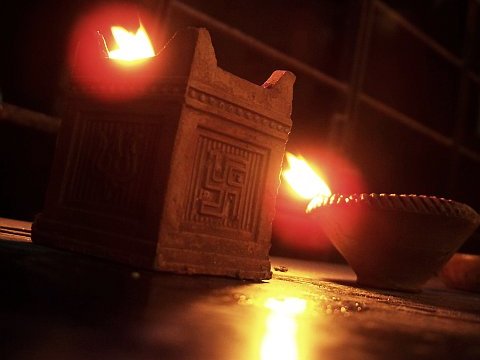 picture of two Deepavali oil lamps, with modern electric lights in the background