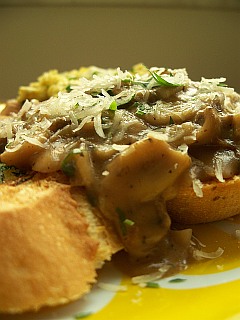 Photo of sauteed mushrooms in a brown sauce poured over thick chunks of toast, garnished with parmesan cheese