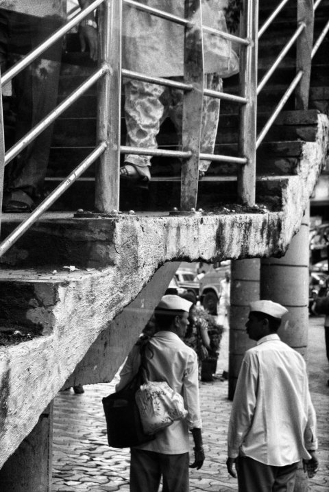 Dabbawalas converse under a footbridge at Charni Road