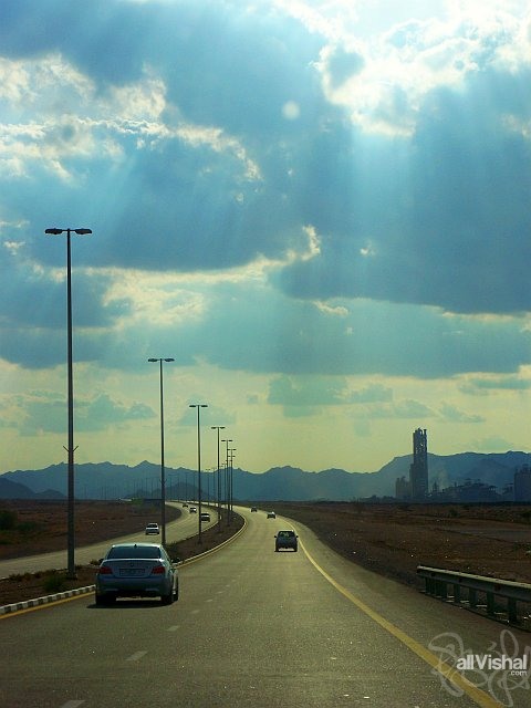 Highway in Fujairah with streams of sunlight coming through the clouds, and a cement factory in the distance