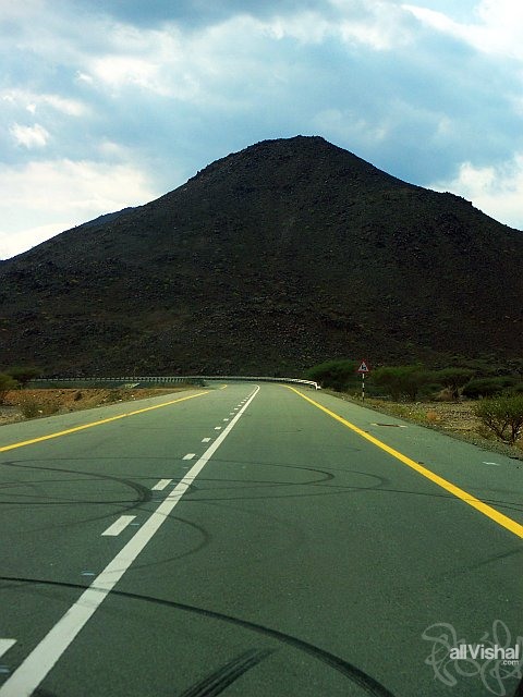 Donut skidmarks on sunny road in front of shadowy mountain in Fujairah