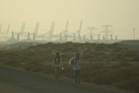 Two men walking with power plant in the bakground, Jebel Ali - before Two men walking with power plant in the bakground, Jebel Ali - before