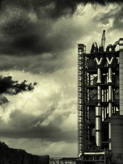 The central column of a cement factory against thick rain clouds, in black & white The central column of a cement factory against thick rain clouds, in black & white