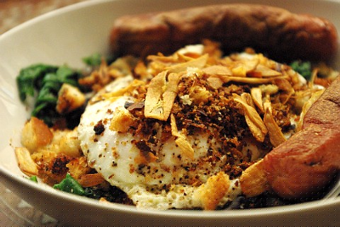 An all day breakfast-esque plate of sausages, spinach, eggs, and crispy fried breadcrumbs